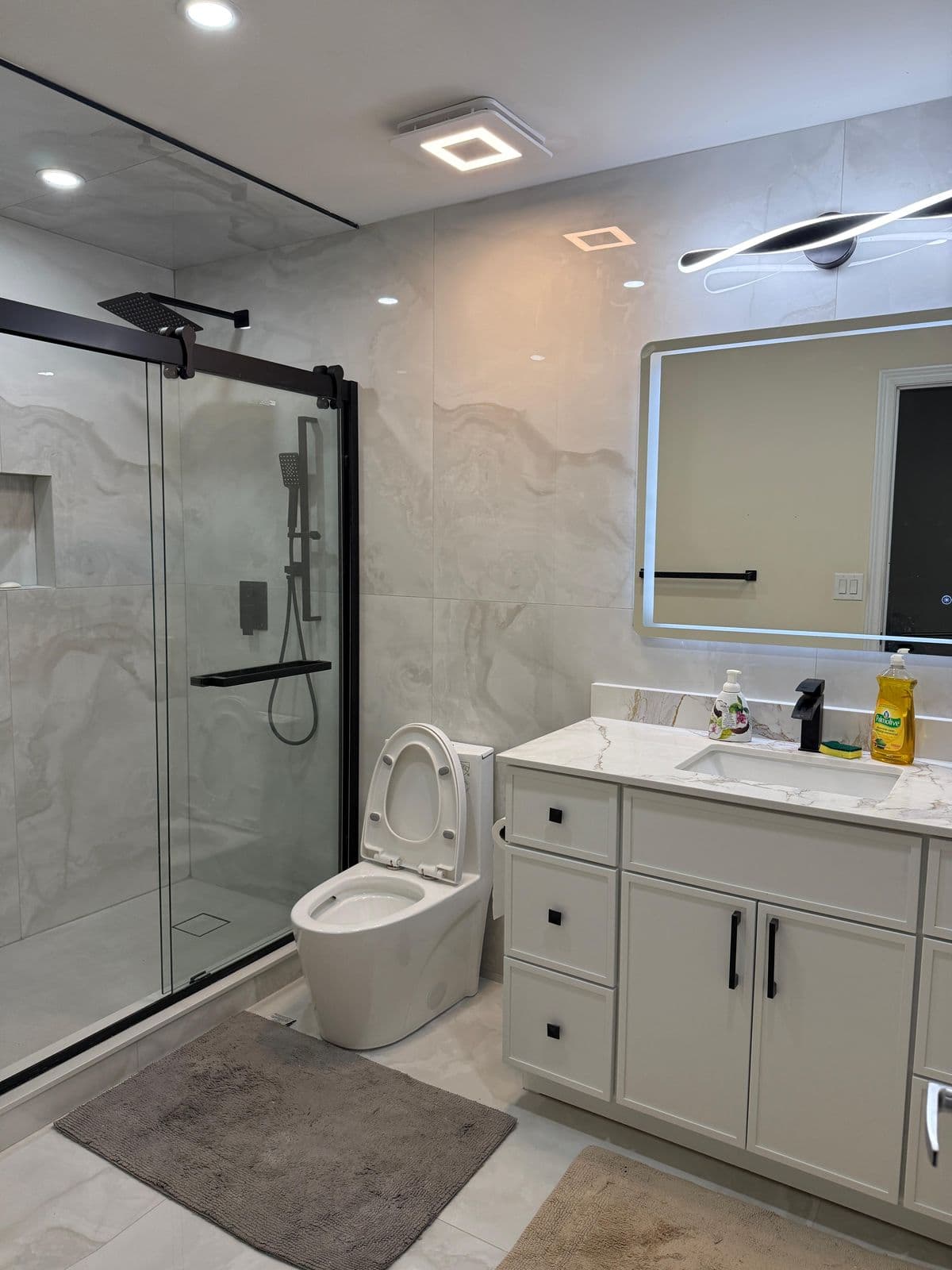 Bathroom renovation with a lit LED mirror, white vanity, and black-frame glass shower in Brampton