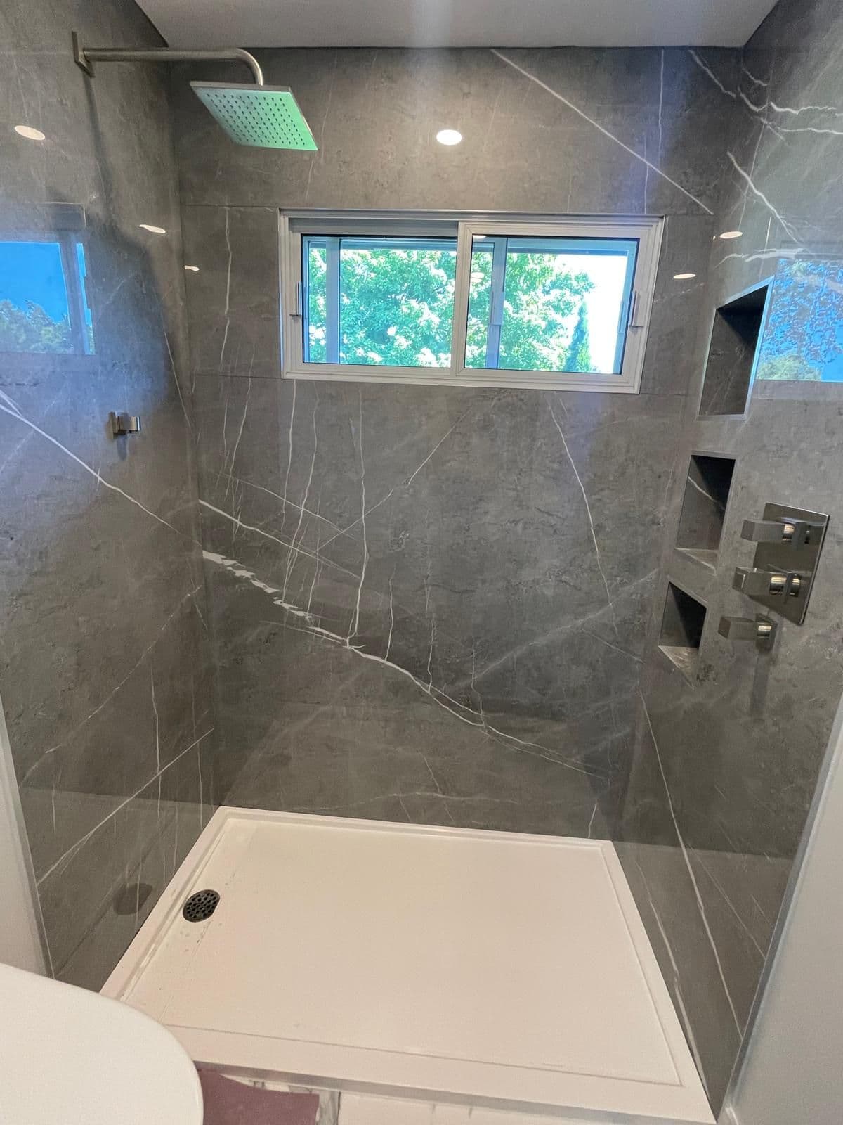Dark grey marble tile shower built around a window with recessed niches, bathroom renovation in Brampton